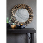 Round mirror with wicker frame on a dark wooden console table against a gray wall.