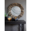 Round mirror with wicker frame on a dark wooden console table against a gray wall.