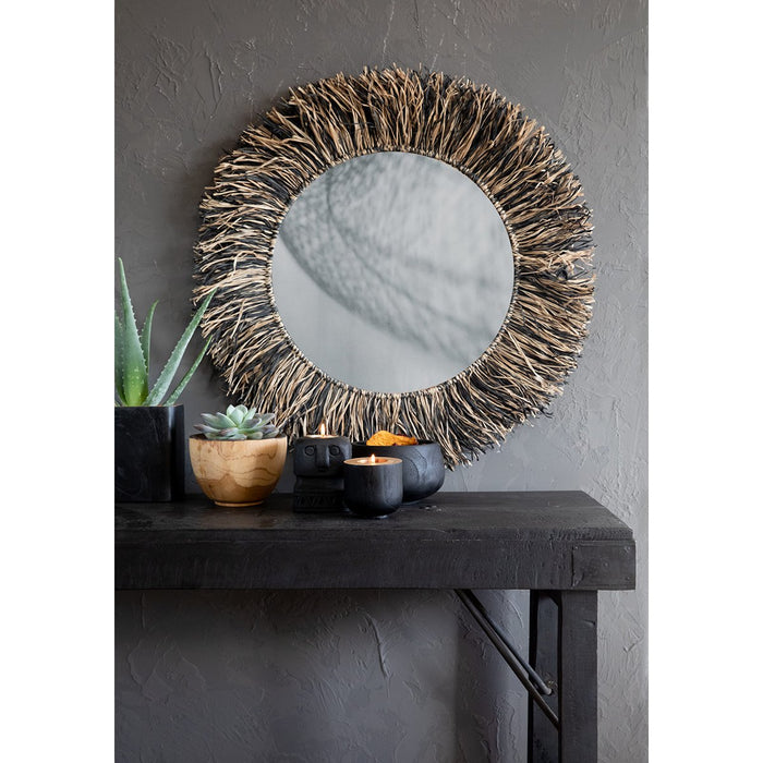 Round mirror with wicker frame on a dark wooden console table against a gray wall.