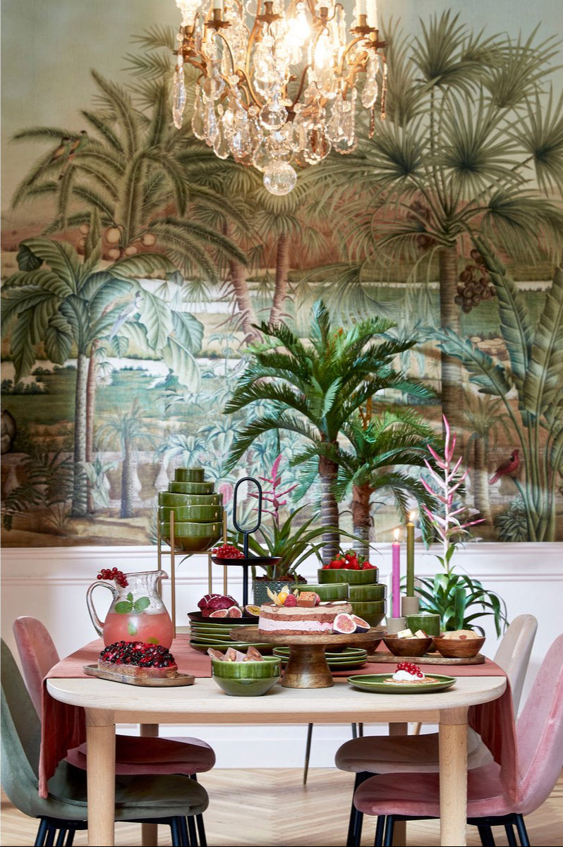 Dining room with tropical mural, table set with fruit and drinks, and pink chairs.