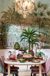 Dining room with tropical mural, table set with fruit and drinks, and pink chairs.