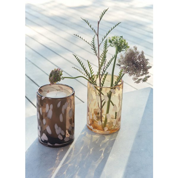 Two glass containers with candles and dried plants on a reflective surface.