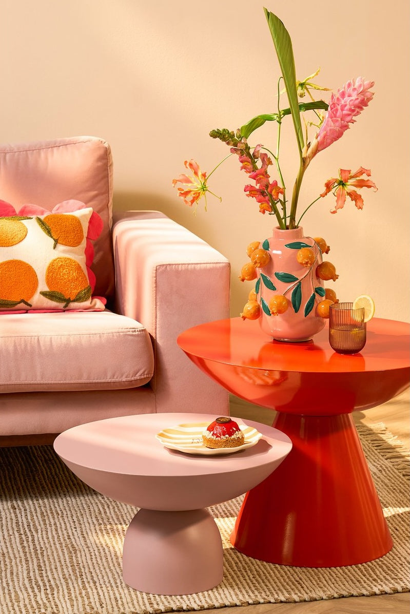 living room with pink couch pink side table orange side table flower vase orange vase