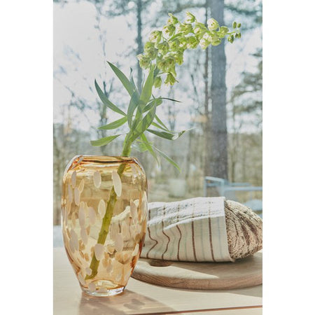 Glass vase with greenery on a table with a blurred outdoor background