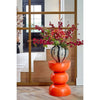 Decorative orange side table with a striped vase and floral arrangement in a room setting.