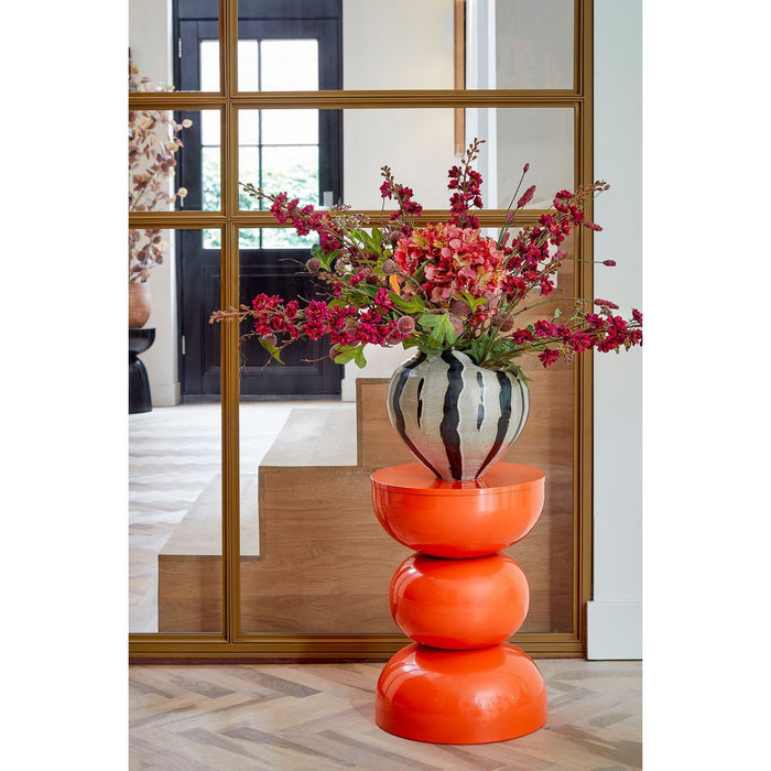 Decorative orange side table with a striped vase and floral arrangement in a room setting.