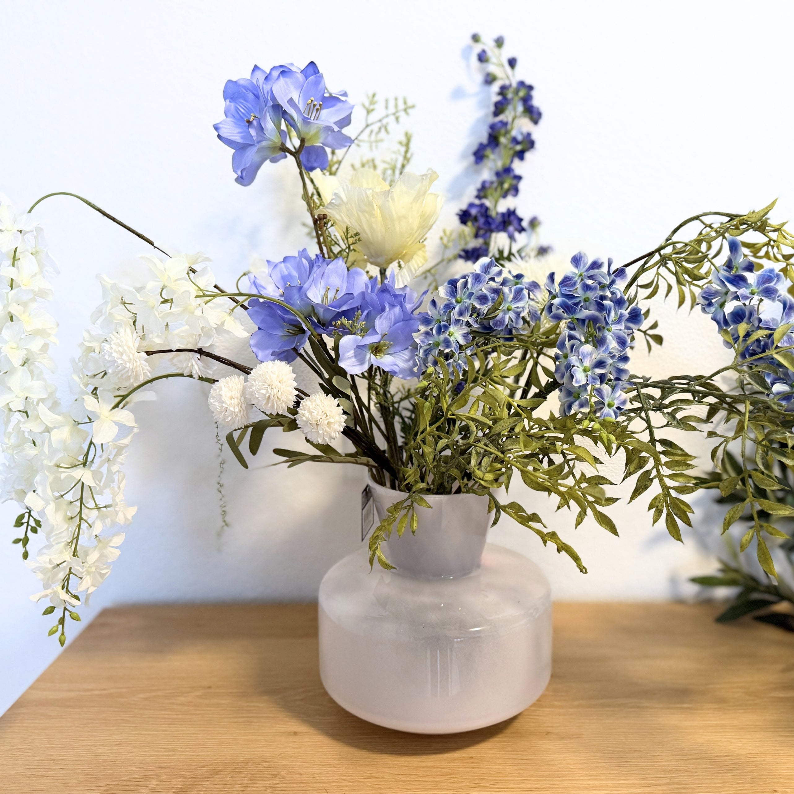 White vase with artificial flowers on a wooden surface