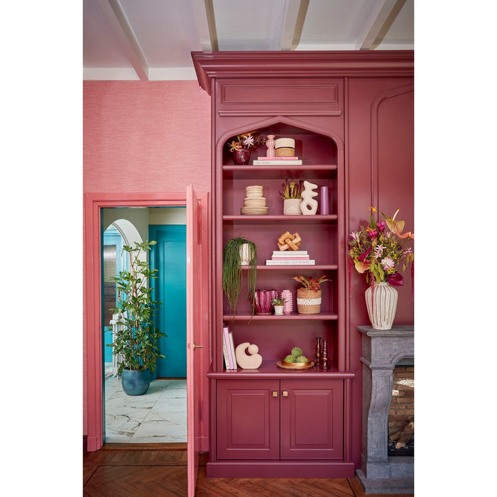 Pink bookshelf with decorative items in a room with a pink wall and blue door.