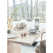 Dining table set with plates, cups, and a vase in an outdoor setting with trees in the background.