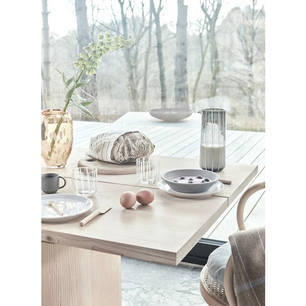 Dining table set with plates, cups, and a vase in an outdoor setting with trees in the background.